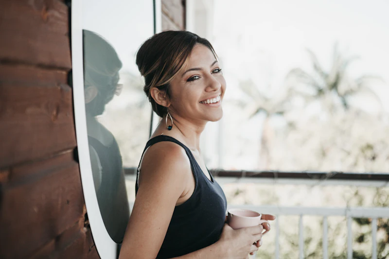 Mulher sorrindo com uma xícara na mão, em uma varanda